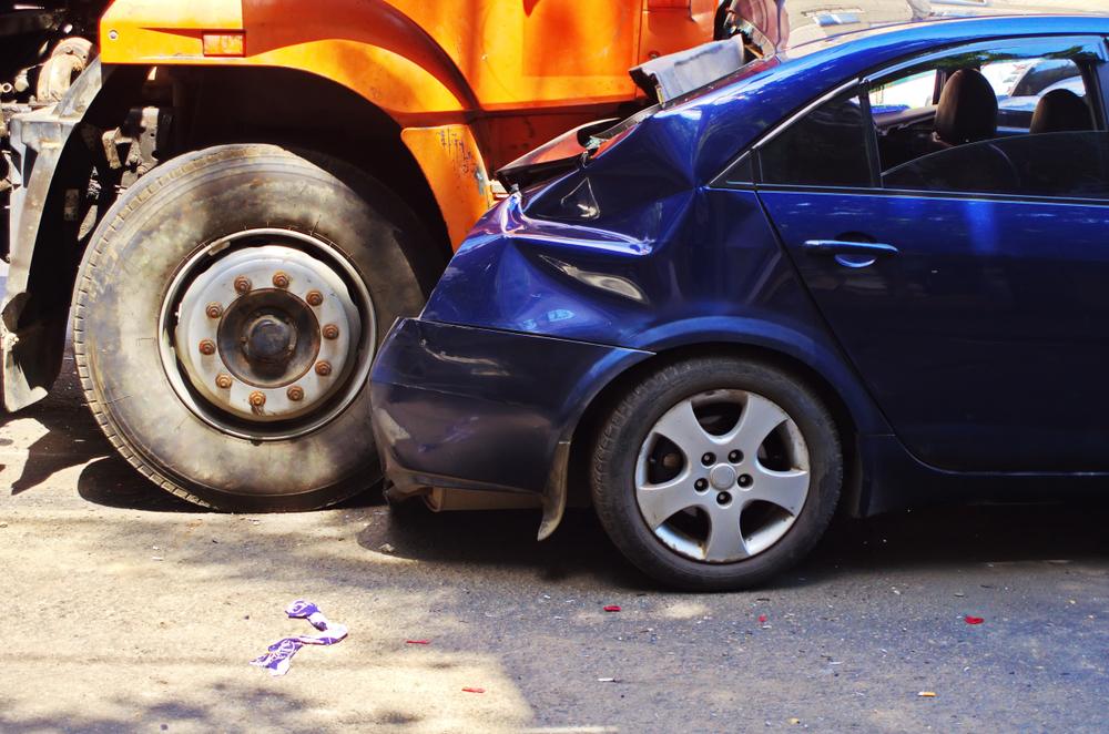 A damaged blue car after a truck crash, whose owner wonders if they can sue a trucking company after an accident.