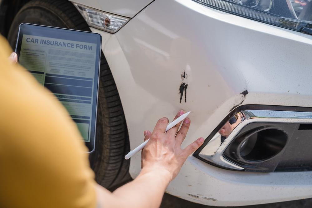A driver checks car damage and completes an accident report after a FedEx truck crash. Victims can file a truck accident claim against FedEx by getting medical care, obtaining a police report, and contacting a lawyer to protect their rights.