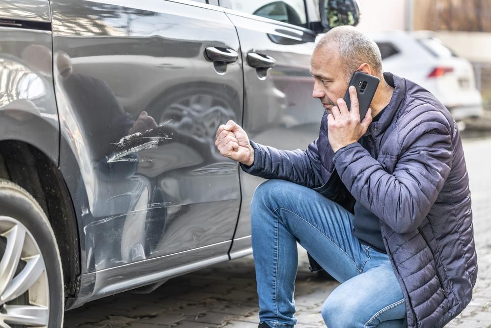 A man kneels next to his car and calls a lawyer after his car accident in North Carolina.