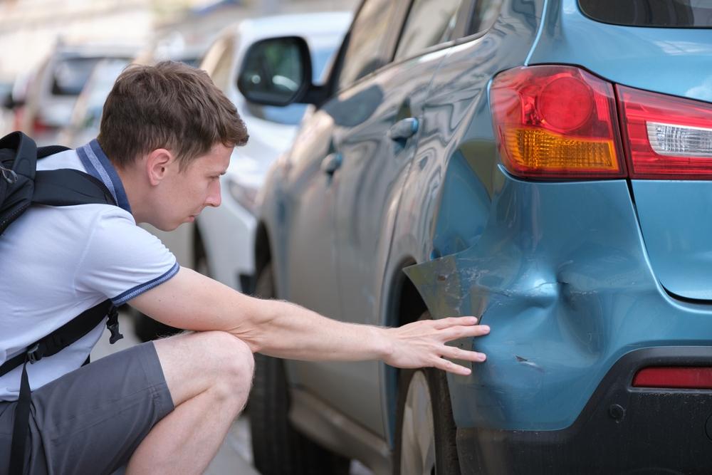 A driver inspects his car after a hit-and-run accident. If you are in a hit-and-run accident, call a personal injury lawyer.