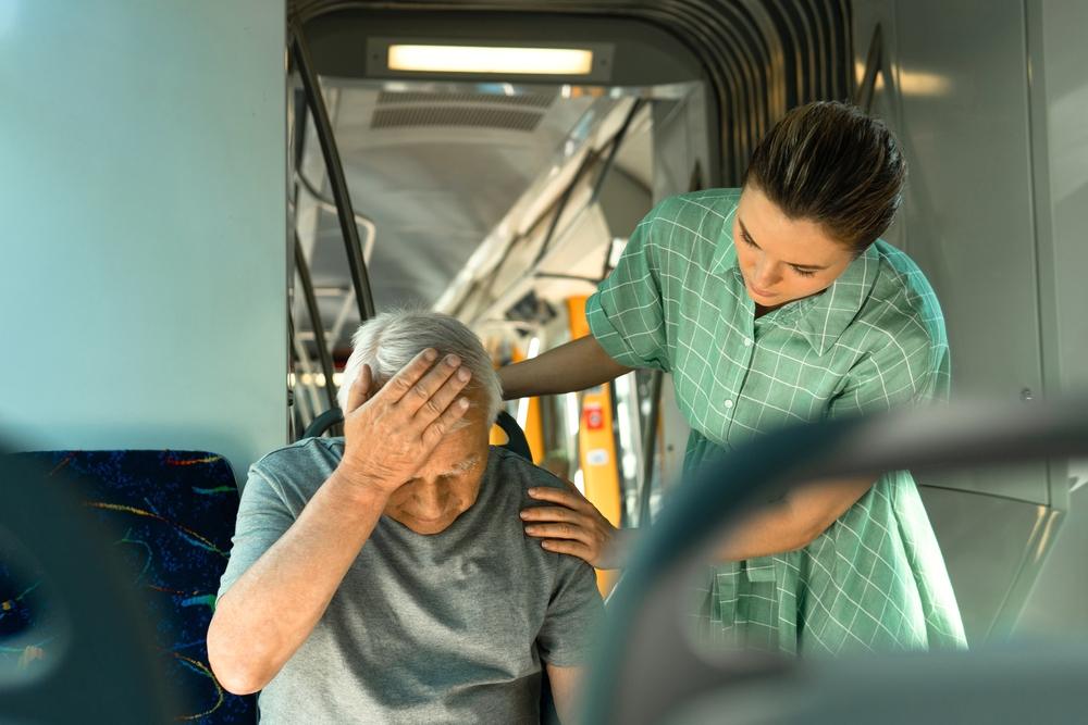 Young woman comforting an old man sitting on a bus who is wondering what he should do after his bus accident injury.
