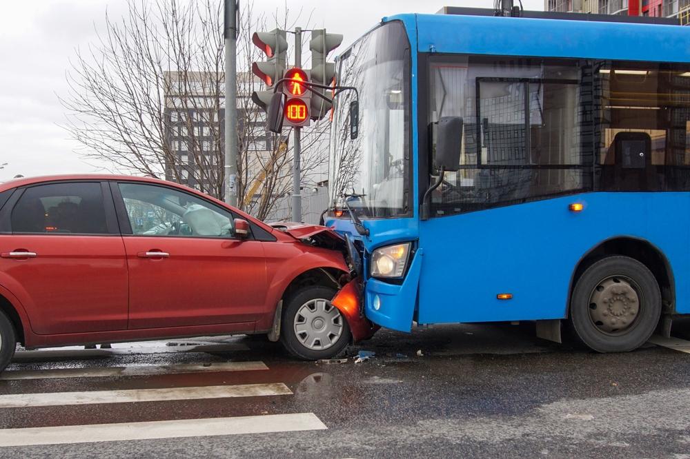 A red car and bus after an accident, as the driver of the car wonders who is responsible if you’re injured in a bus accident.