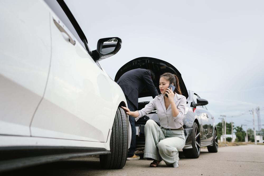 A woman and a man inspecting their cars after an auto accident, with both wondering how to get a crash report in Asheboro, NC