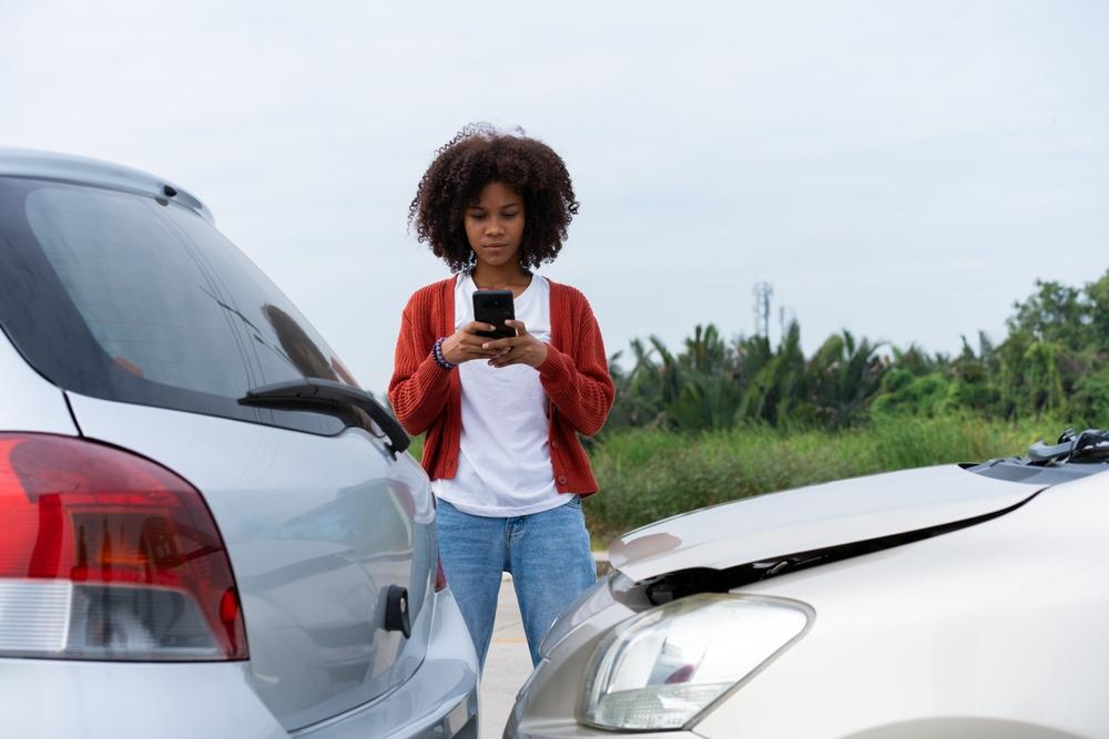 A woman standing by her car after a crash and using her phone to try to figure out how to get a crash report in Kannapolis, NC.