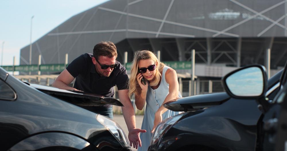 Two people at the scene of a car accident, with one person calling an insurance company about the incident and unsure of how to get a crash report in Winston-Salem, NC