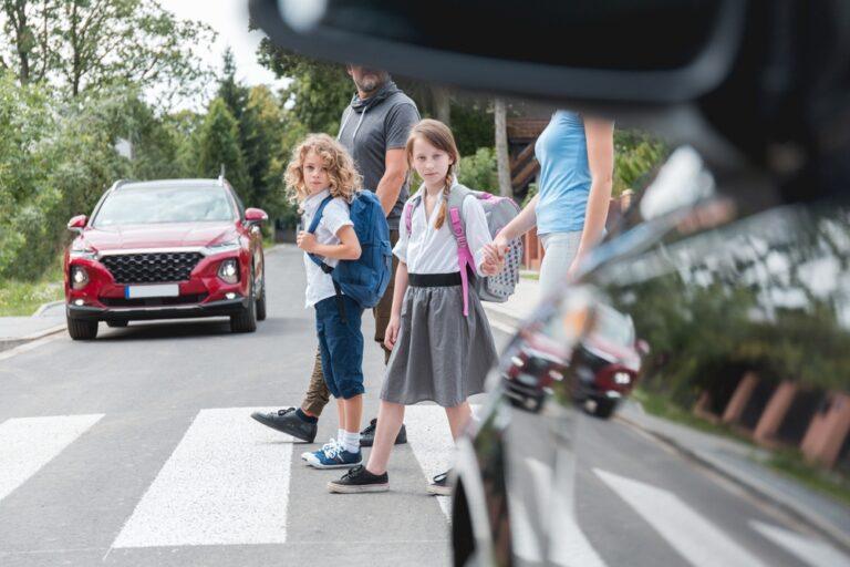 A couple leading two children out of the car and onto the sidewalk. Learn some back-to-school safety tips for drivers, parents, and students.