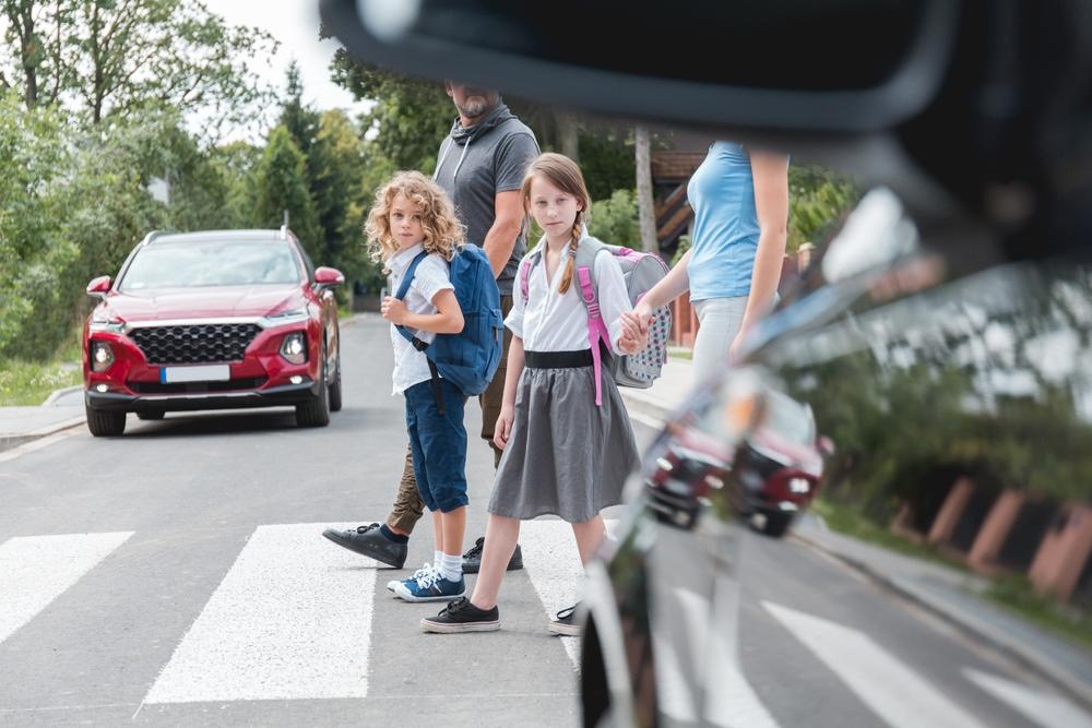 A couple leading two children out of the car and onto the sidewalk. Learn some back-to-school safety tips for drivers, parents, and students.